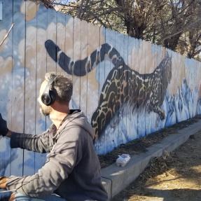 Artist painting a cheetah on the side of a fence