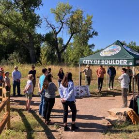 People standing around a city of boulder tent on a trail outside.