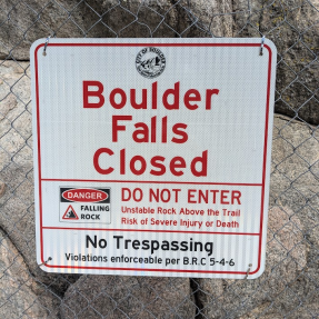 Sign on a chain-link fence saying "Boulder Falls Closed"