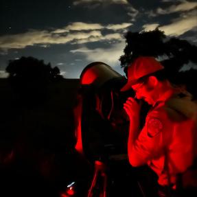 Ranger looking through the lens of a telescope on a dark night