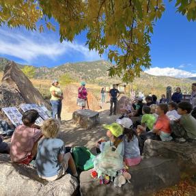 Group of young people sitting outside on rocks listening to adults speak