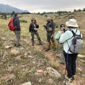 Five people on a trail in the foothills use small hand-held tools and discuss.