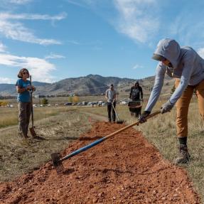 Person uses rake to smooth new trail soil.