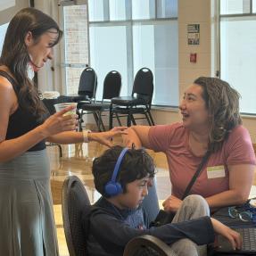 Right profile of city staff member, standing talking with community member sitting at table with son