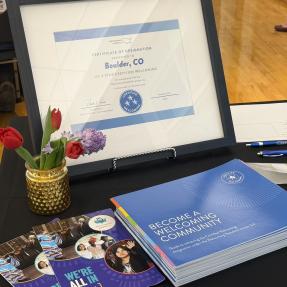 Certificate of designation framed on welcome table next to a pot of flowers and information packets