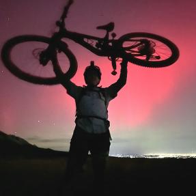 Person holds bike above their heads with northern lights in background