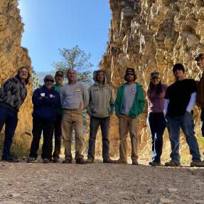 A group of people pose for a team photo on a trail in front of some cliffs.