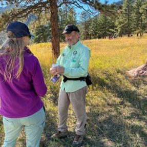 Man wearing volunteer shirt explains something to a woman hiking.