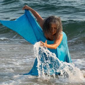 Afro-Brazilian dancer wearing a flowy blue dress in the waves 