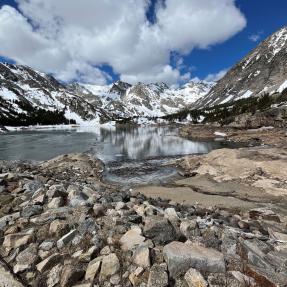 dry rocks along mountain lake that isn't filled up under gray and snow-specked mountain 