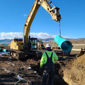 Crane lifting plastic piping to be lowered into the ground
