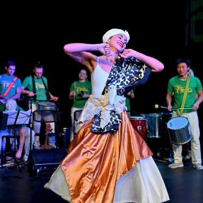 Afro-Brazilian dancer on stage with musicians in the background.