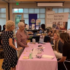 Two older adult women speaking with outreach staff during an assistive technology fair. 