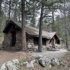 Green Mountain Lodge, stone building surrounded by pine trees with a stone patio and picnic tables.