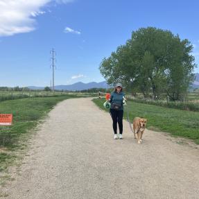 Woman carrying two poop bags to a trash can while holding her dog on leash.