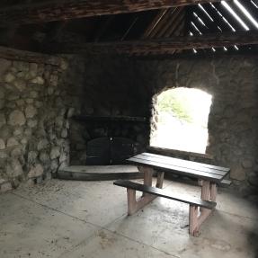 Inside the Stone Shelter, the east side has a picnic table and non-operational fireplace in the corner.