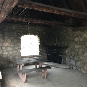 Inside the Stone Shelter, the west side has a picnic table and non-operational fireplace in the corner.