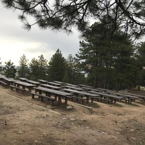 Rows of picnic tables heading slightly downhill, viewed from the doorway of the Stone Shelter.