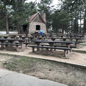 Rows of picnic tables heading slightly uphill with the Stone Shelter and pine trees in the background.
