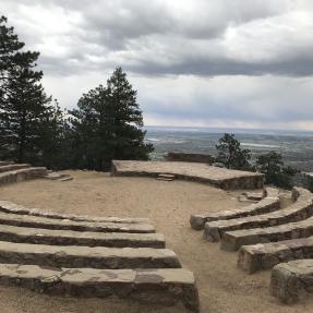 Stone seating circling down toward the center of Sunrise Amphitheater with Boulder down below.