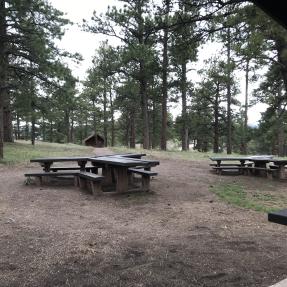 Looking west from inside Wood Shelter, there are two large picnic tables and a path to the restroom.