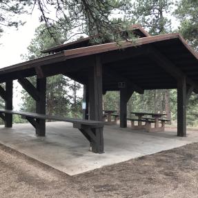 The Wood Shelter with two picnic tables on one side and a counter-height serving table on the other.