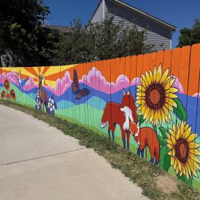 Artist painting a colorful mural with foxes and sunflowers on a public facing fence