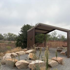 Beautiful shelter with carved metal sides and a rock seating area outside at Sawhill Ponds.