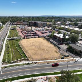 Aerial view of the flood channel along the roadway at left, next to a cleared dirt lot, a parking area, and a multistory building under construction.
