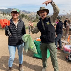 Someone enthusiastically pointing at another person holding a bunch of poop bags and orange flags.