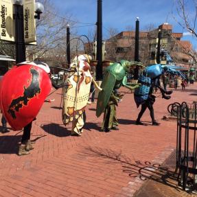 People marching down the Pearl Street Mall in colorful beetle costumes