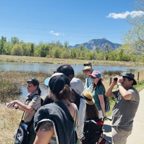 A group of people stand next to a pond on a clear sky day while one person holds an animal skull.