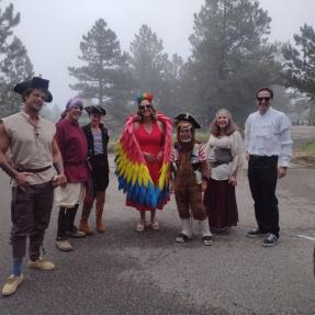 A group of people standing in a parking lot wearing pirate and parrot costumes.